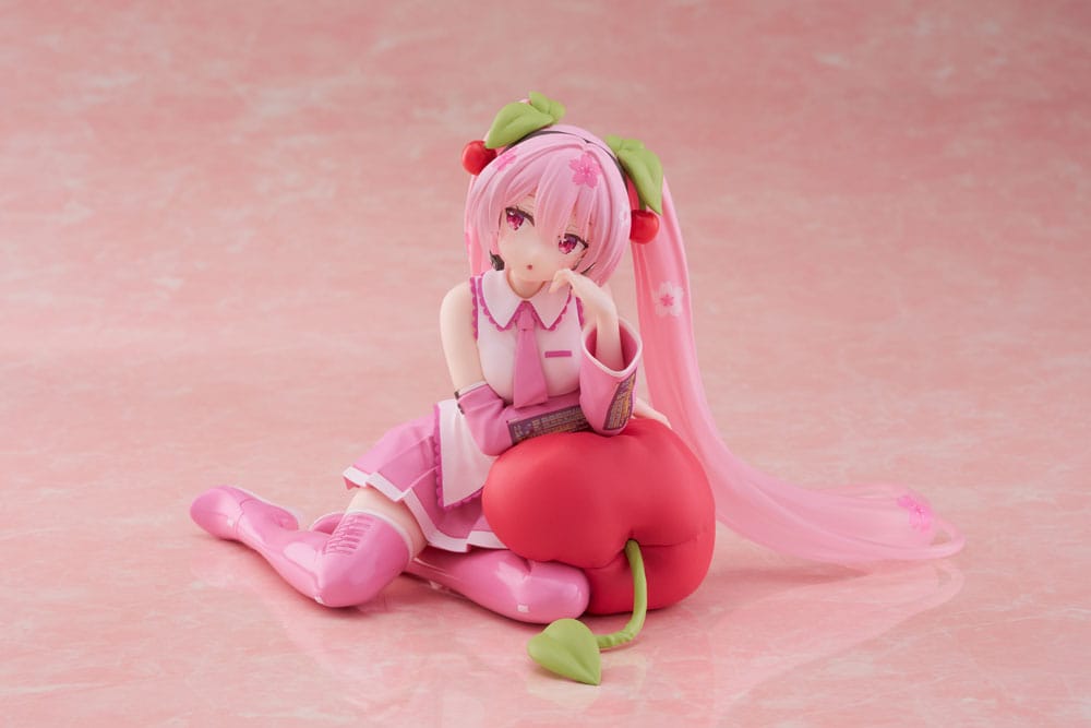 Figurine Sakura Miku Cherry Cushion Ver. de 13 cm, assise contre un coussin cerise, cheveux roses décorés de fleurs et cerises, tenue rose détaillée et expression douce.