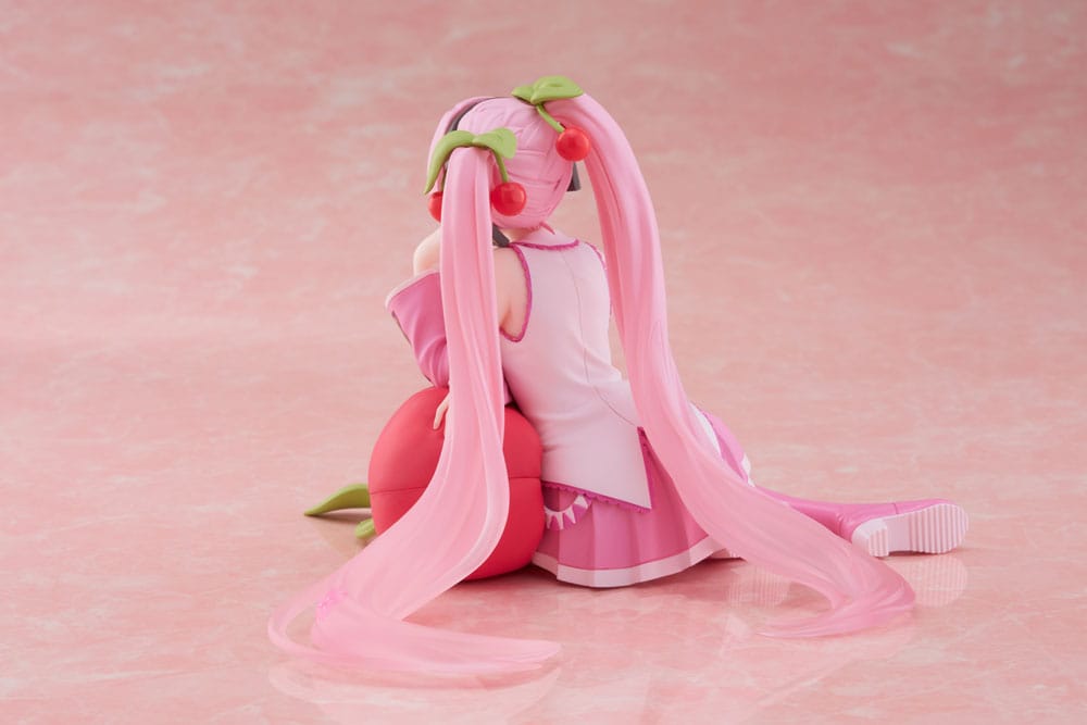 Figurine Sakura Miku Cherry Cushion Ver. de 13 cm, assise contre un coussin cerise, cheveux roses décorés de fleurs et cerises, tenue rose détaillée et expression douce.