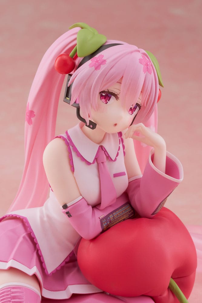 Figurine Sakura Miku Cherry Cushion Ver. de 13 cm, assise contre un coussin cerise, cheveux roses décorés de fleurs et cerises, tenue rose détaillée et expression douce.